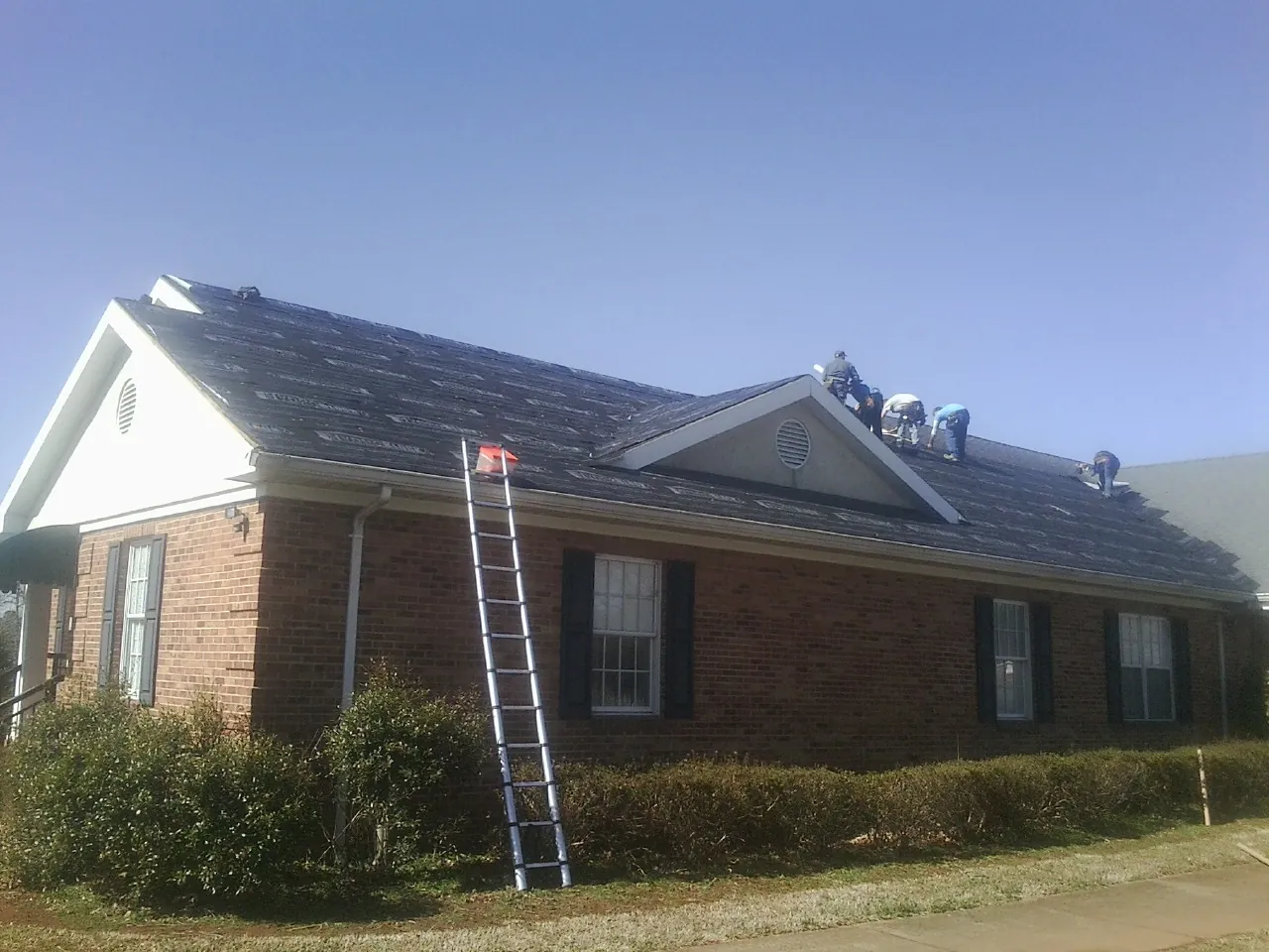 Crew tearing shingles off a brick ranch roof with a ladder set — Metal Roof Repair work by our crew in Yemassee