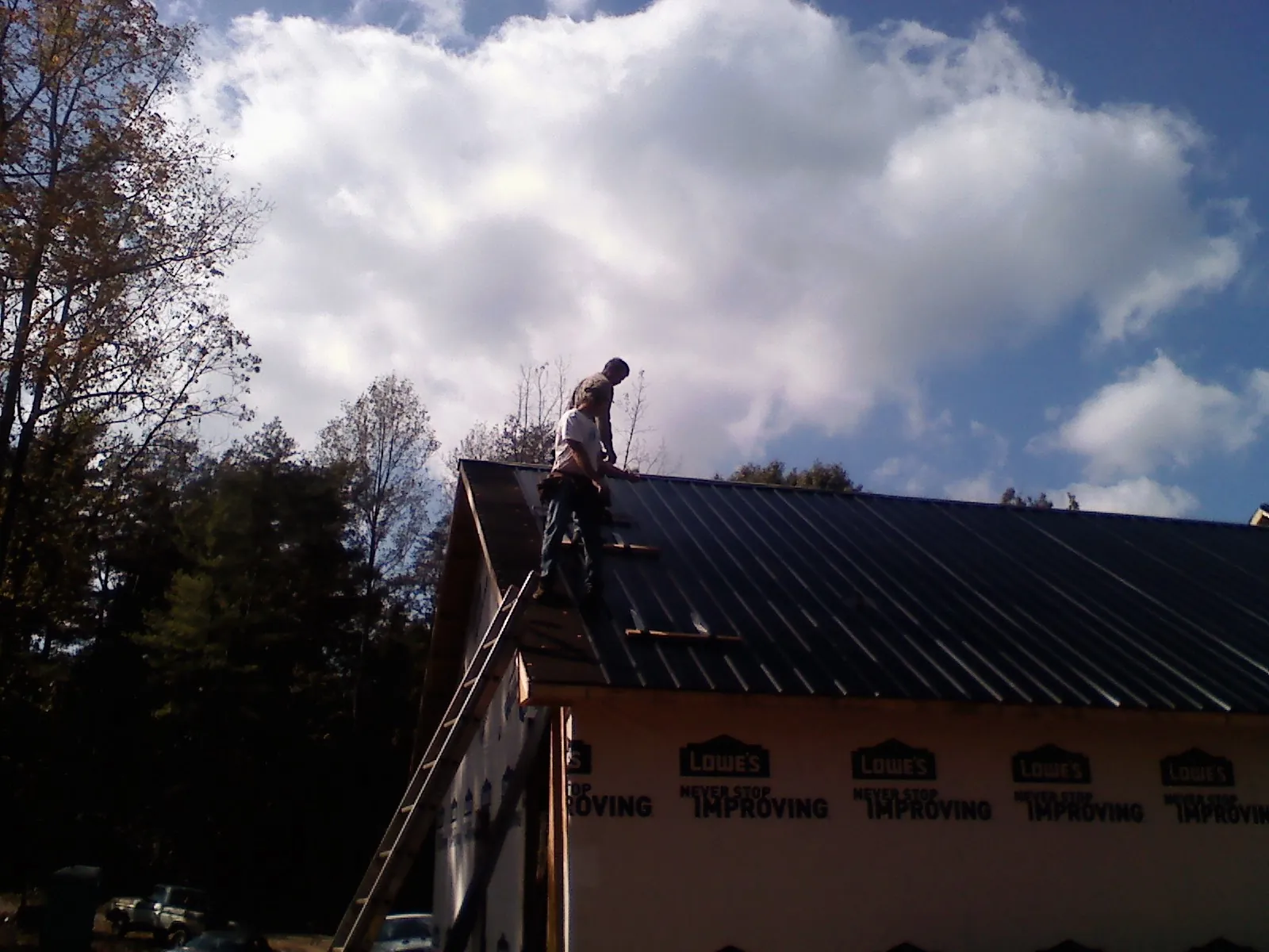 Roofer fastening dark metal panels high against a cloudy sky, from a Roof Inspection job in Yemassee