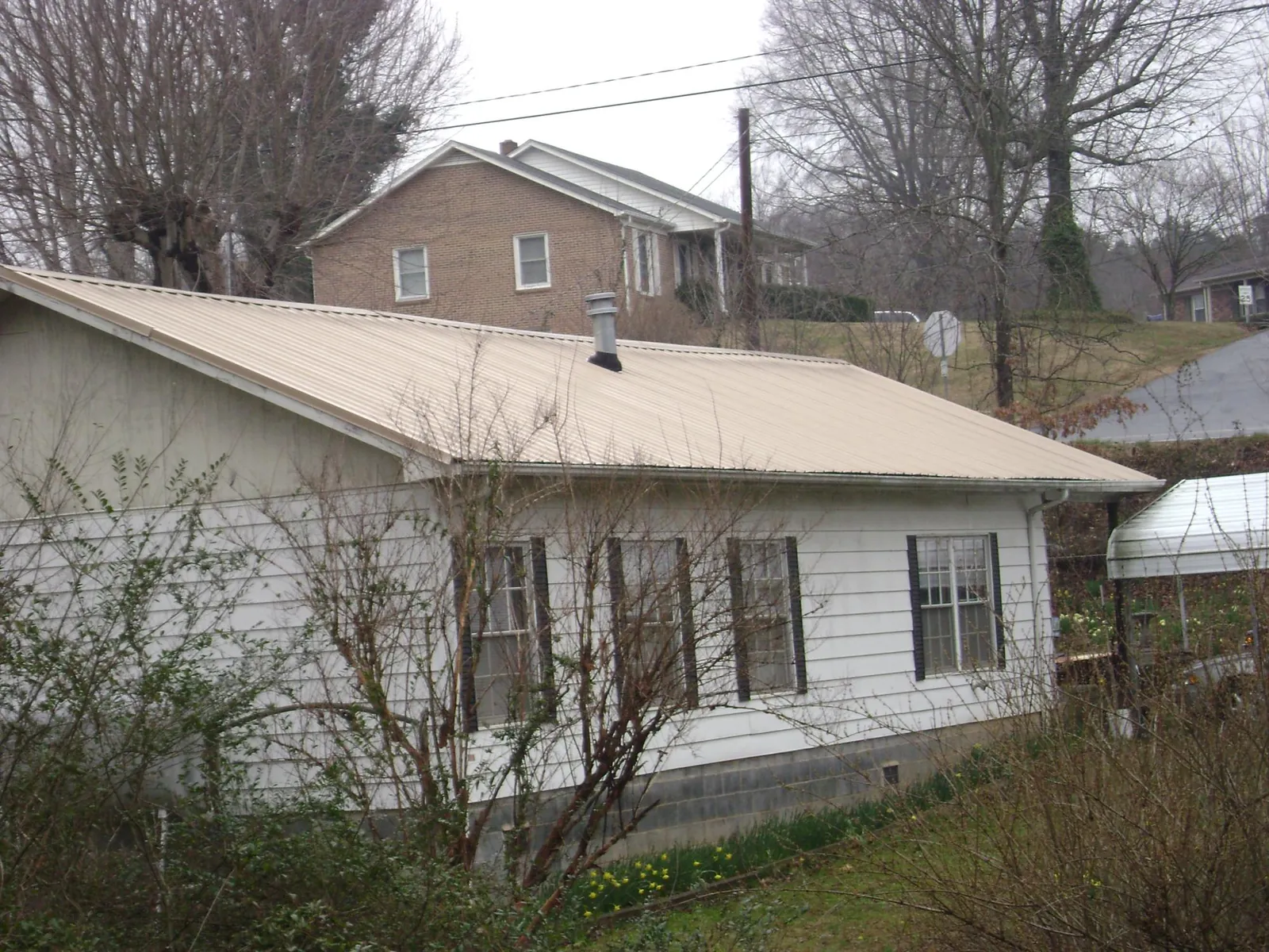 Tan metal roof on a white sided house set into a hillside — Commercial Roofing by Roofing Brothers in Yemassee